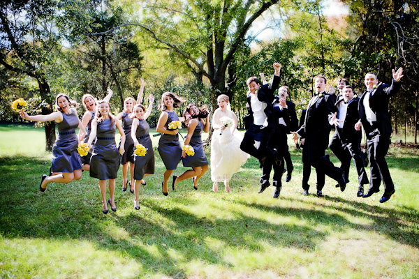 the classic wedding party jumping in the air pose - bridesmaids are wearing purple dresses with yellow bouquets, bride is wearing white dress, and groomsmen are wearing black and white suits - photo by North Carolina based wedding photographers Cunningham Photo Artists
